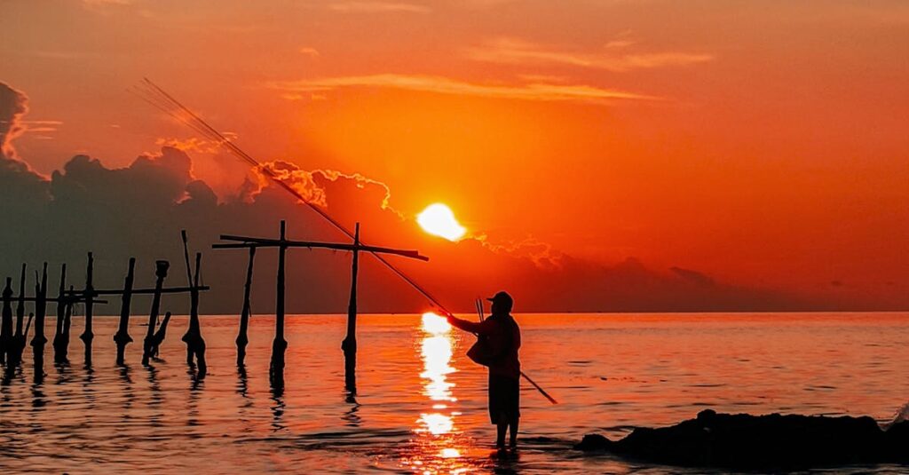Silhouetted fisherman with fishing rod at sunset on Lombok coast, Indonesia.
