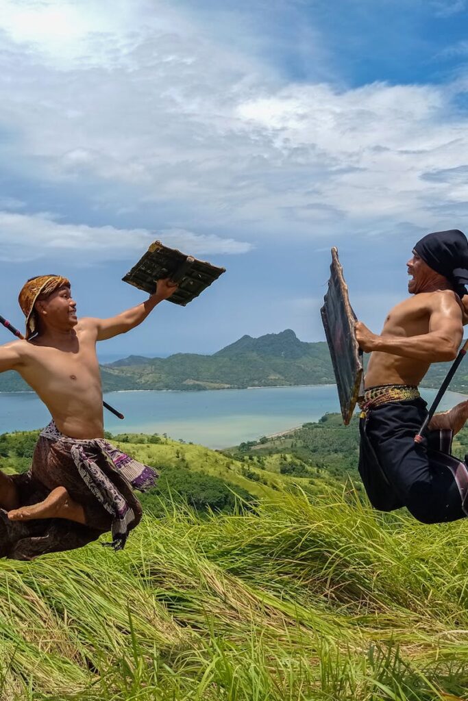 Men in a traditional Sasak warrior dance, leaping midair in scenic Lombok, Indonesia.