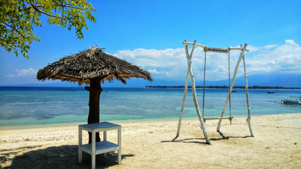 Tranquil beach scene with a swing and thatched umbrella in West Nusa Tenggara, Indonesia.